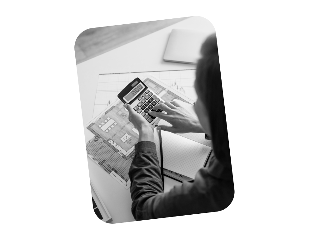 Person nutzt Taschenrechner über Bauplänen mit Notizbuch auf Tisch