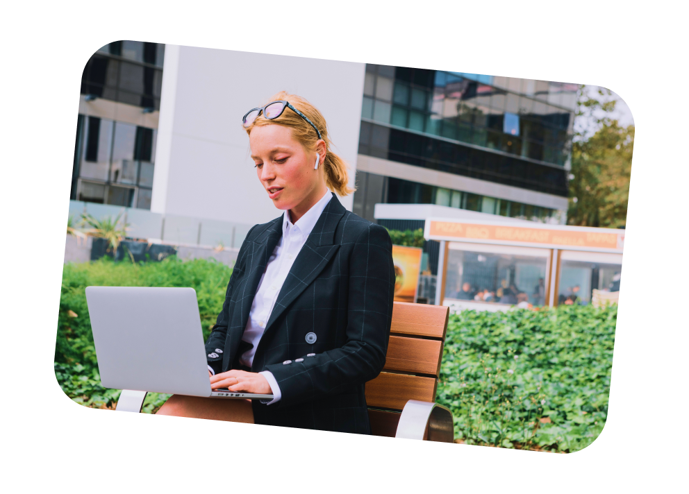 Geschäftsfrau mit Brille auf dem Kopf arbeitet draußen an Laptop auf Parkbank