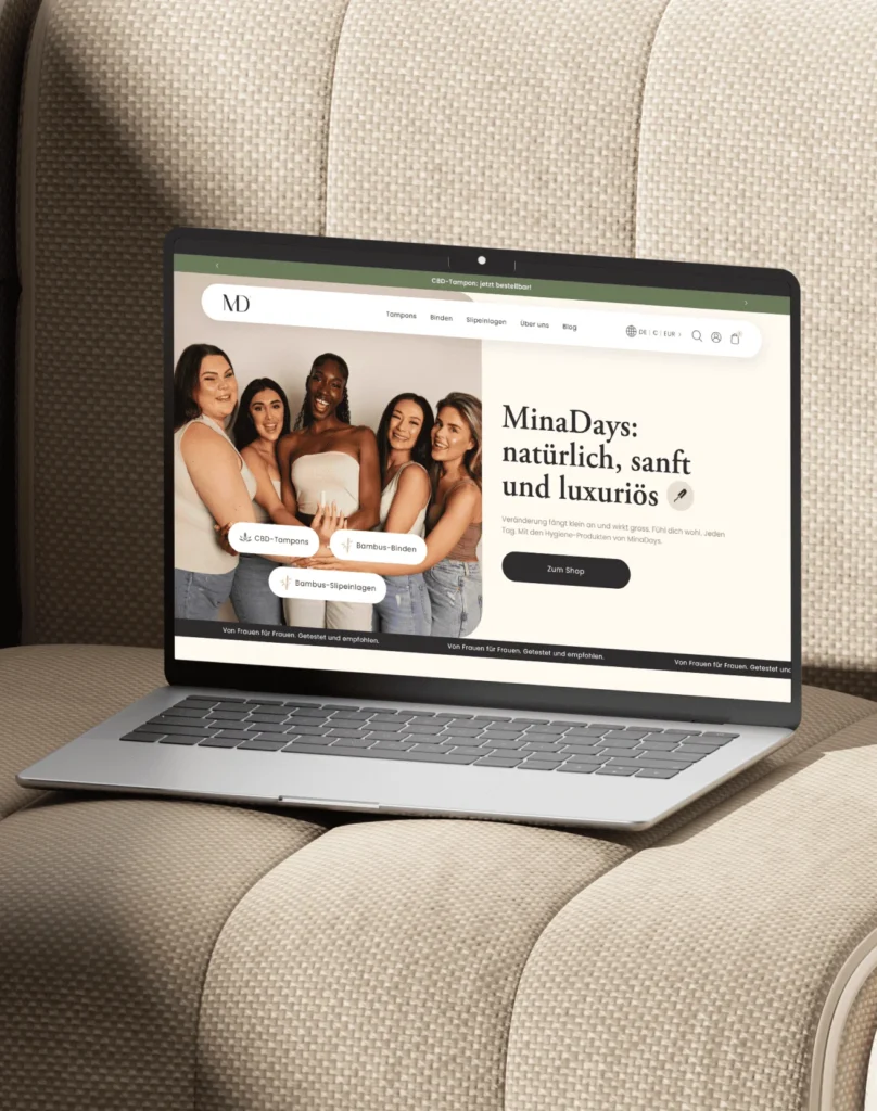 Laptop auf einem gesteppten Stuhl zeigt die Website von MinaDays mit fünf Frauen und Produktnamen wie CBD-Tampons und Bambus-Binden