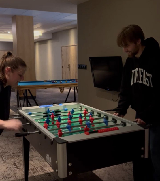 Zwei junge Menschen spielen Tischfußball in einem gemütlichen Raum mit Billardtisch im Hintergrund