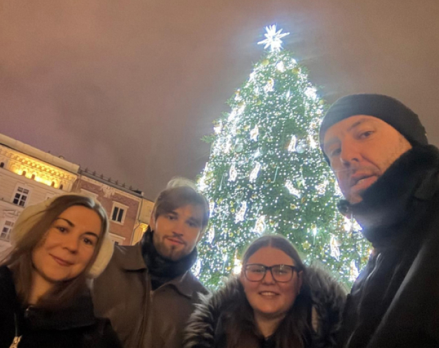 Vier Personen vor einem festlich geschmückten, beleuchteten Weihnachtsbaum in der Nacht